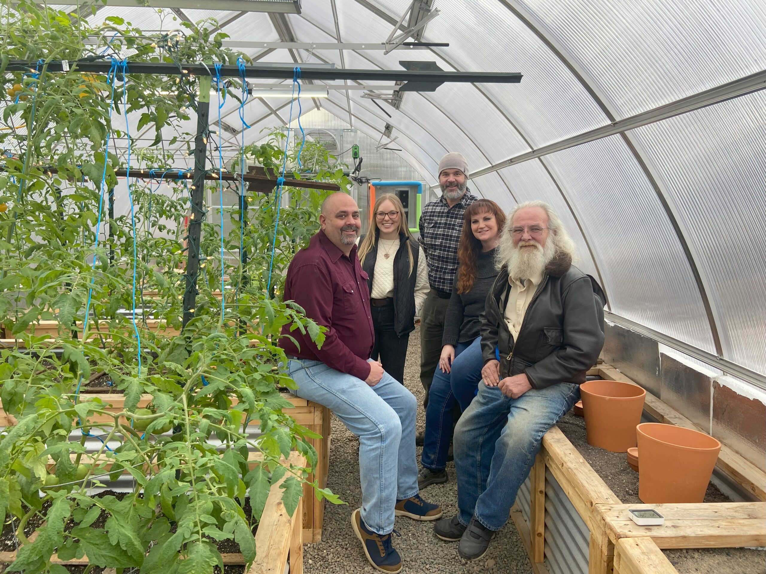The POIC team sitting on raised beds filled with tomato plants inside the proof-of-concept greenhouse.